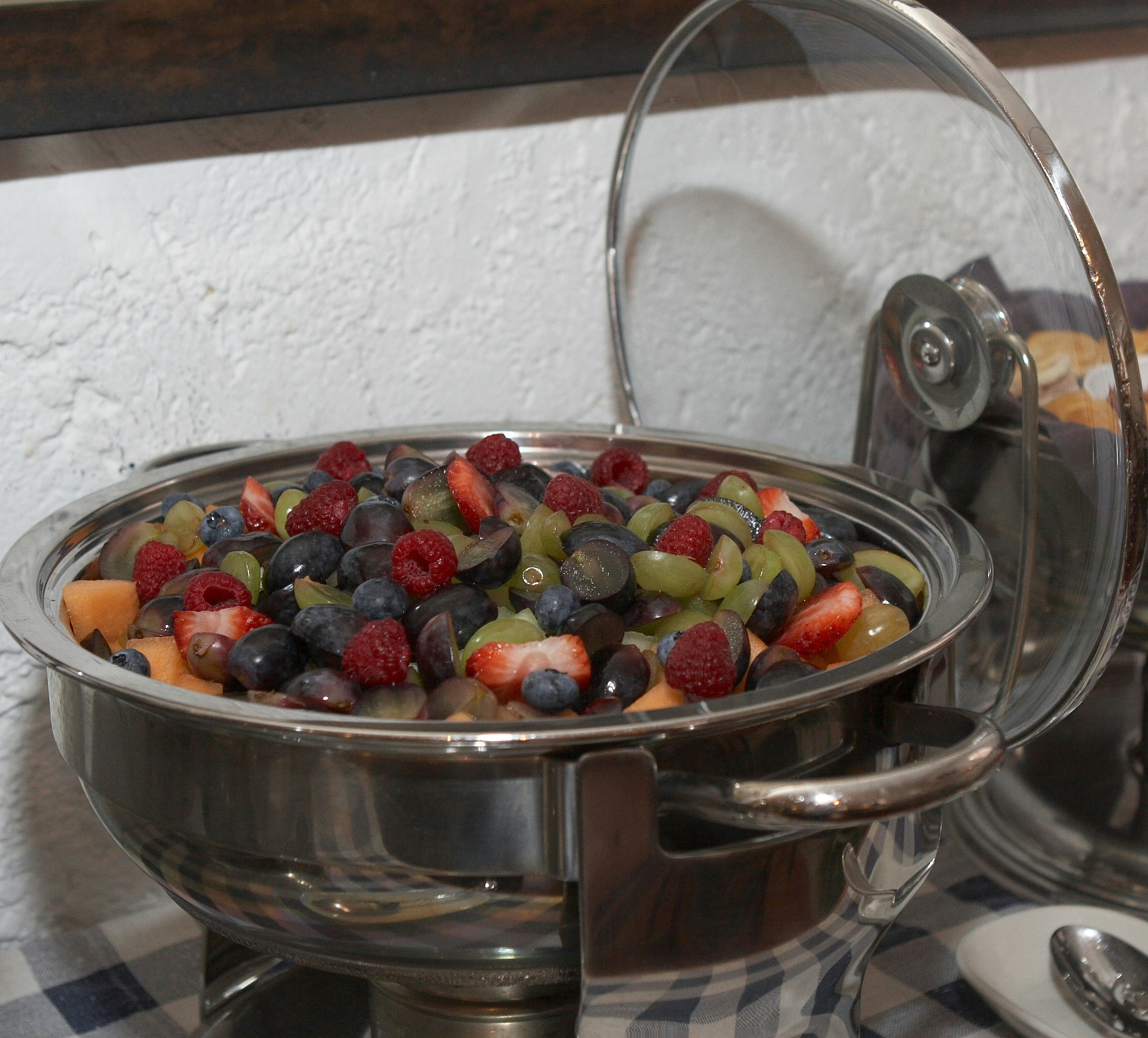 Grapes, raspberries and cantaloupe in a metal serving bowl with hinged clear lid