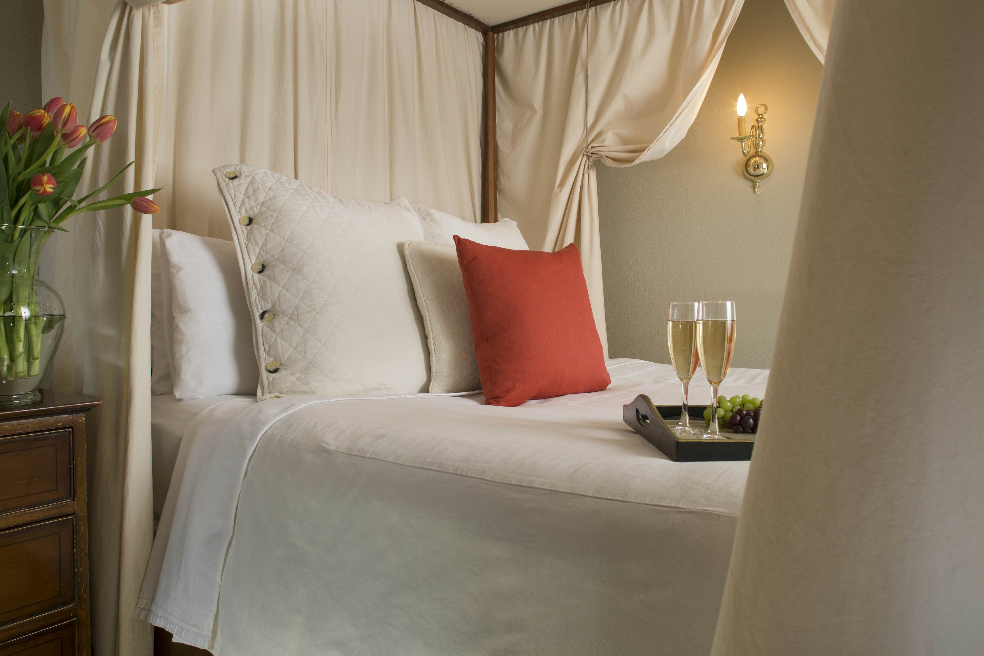 Close up of canopied four-poster bed with decorative pillows and tray with two champagne flutes