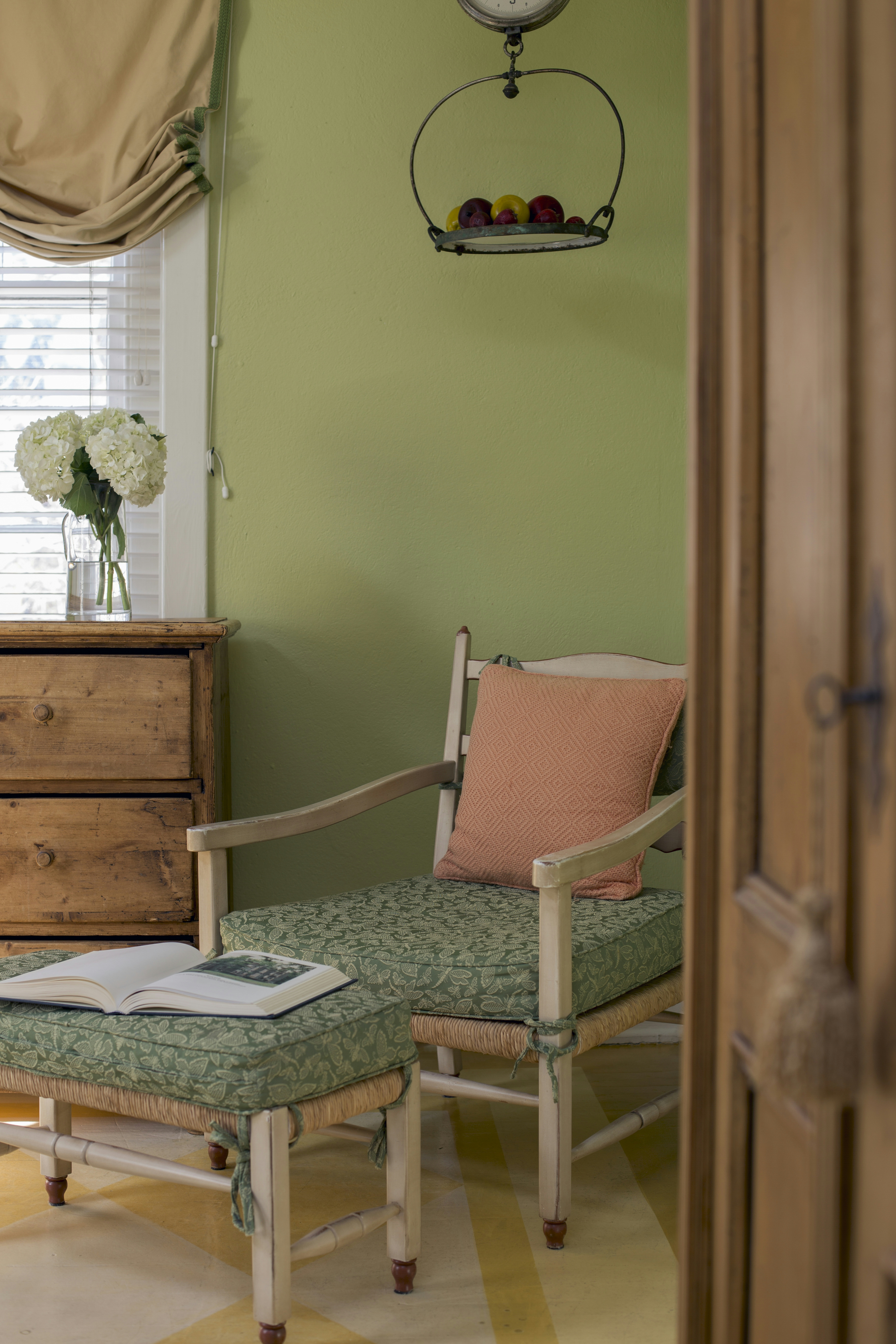 Wooden painted chair with cushions and matching footstool in corner of bedroom