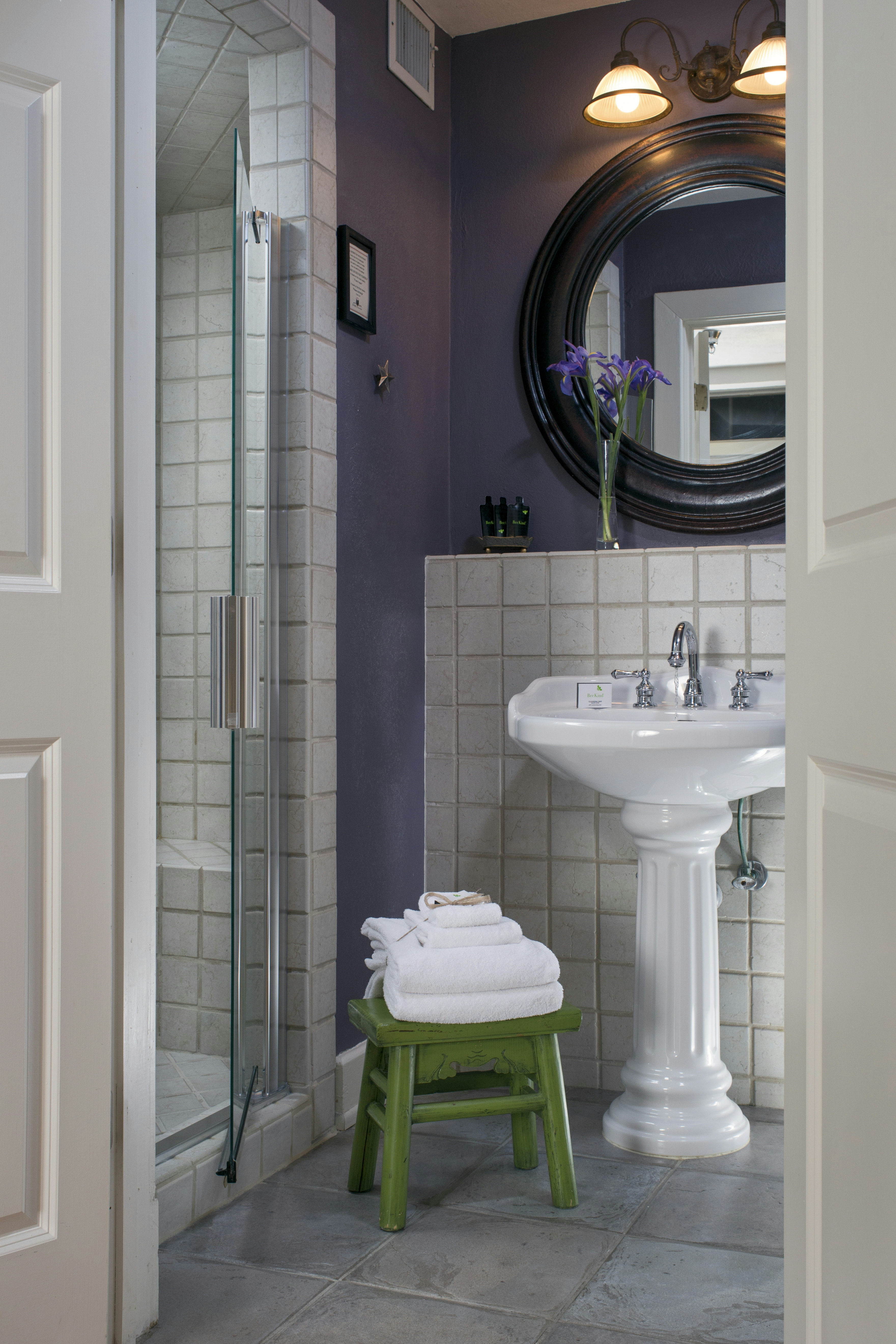 Bathroom with lavender walls, white pedestal sink, framed mirror, and tiled shower with glass doors