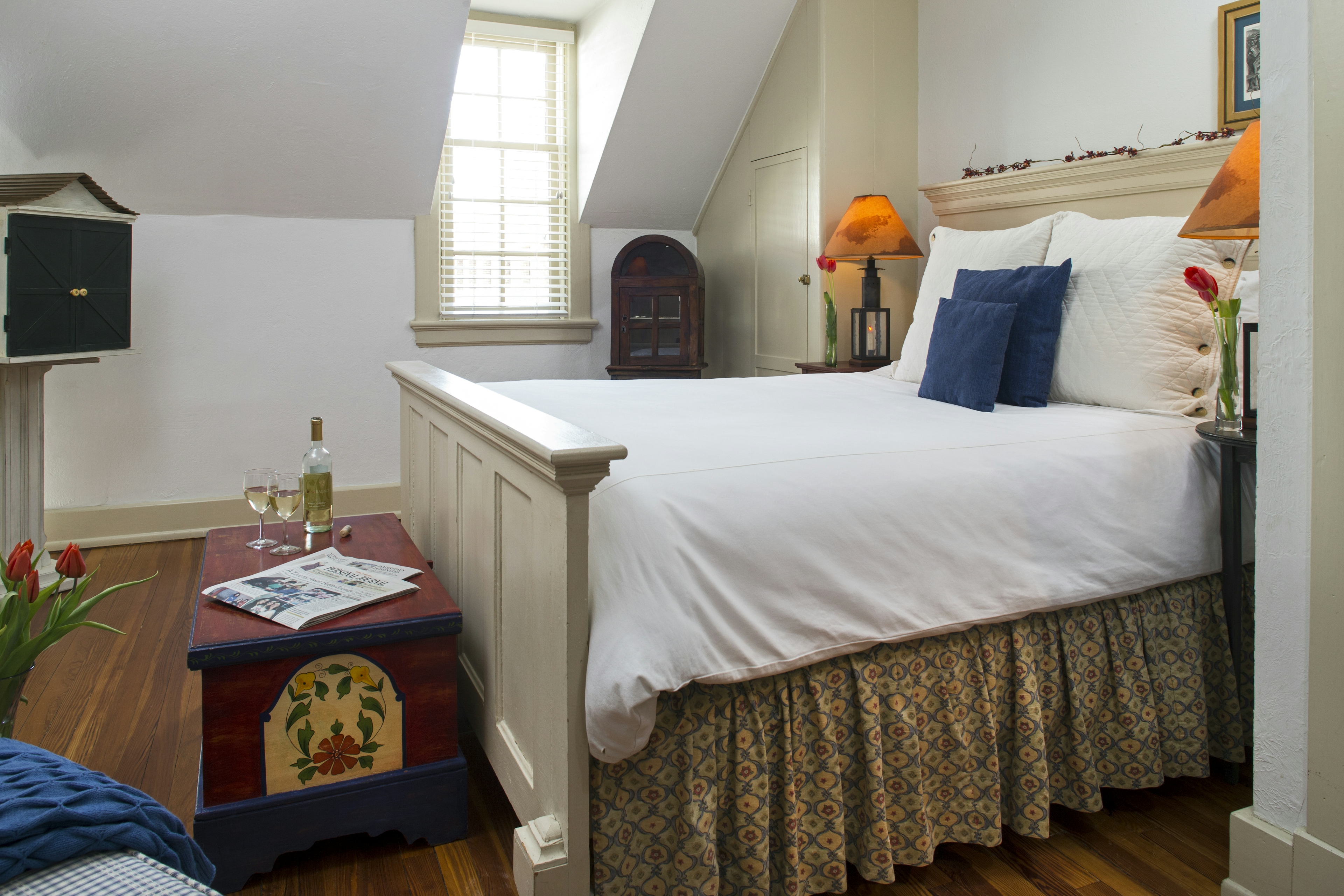 Inviting bed with headboard & footboard constructed of wooden doors, matching nightstands with lamps, and folk-art painted chest at foot of bed