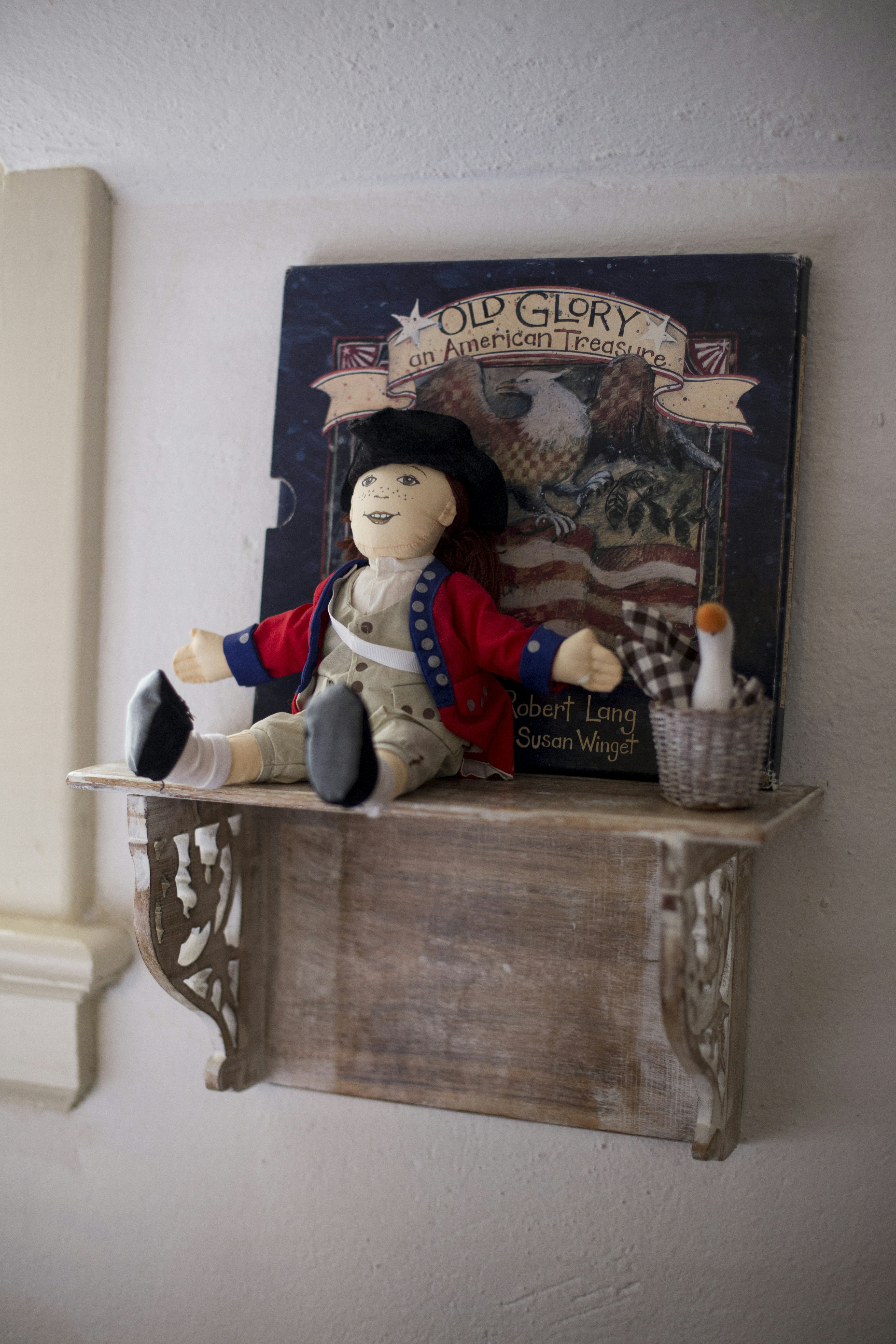 Decorative shelf with Americana items, colonial doll, basket, and Old Glory book