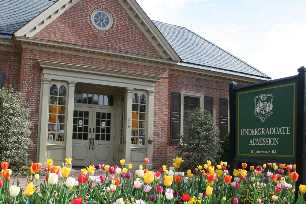 Brick admissions building with tan trim with green admissions sign in front yard with many multicolor tulips