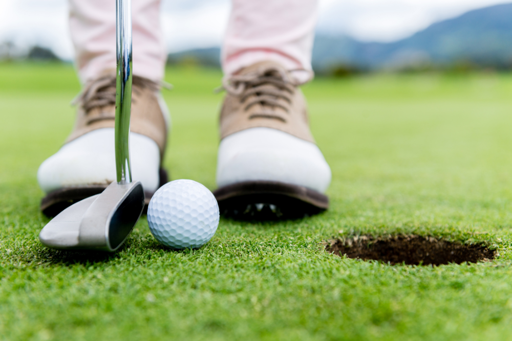 Man in golf shoes with putter near hole