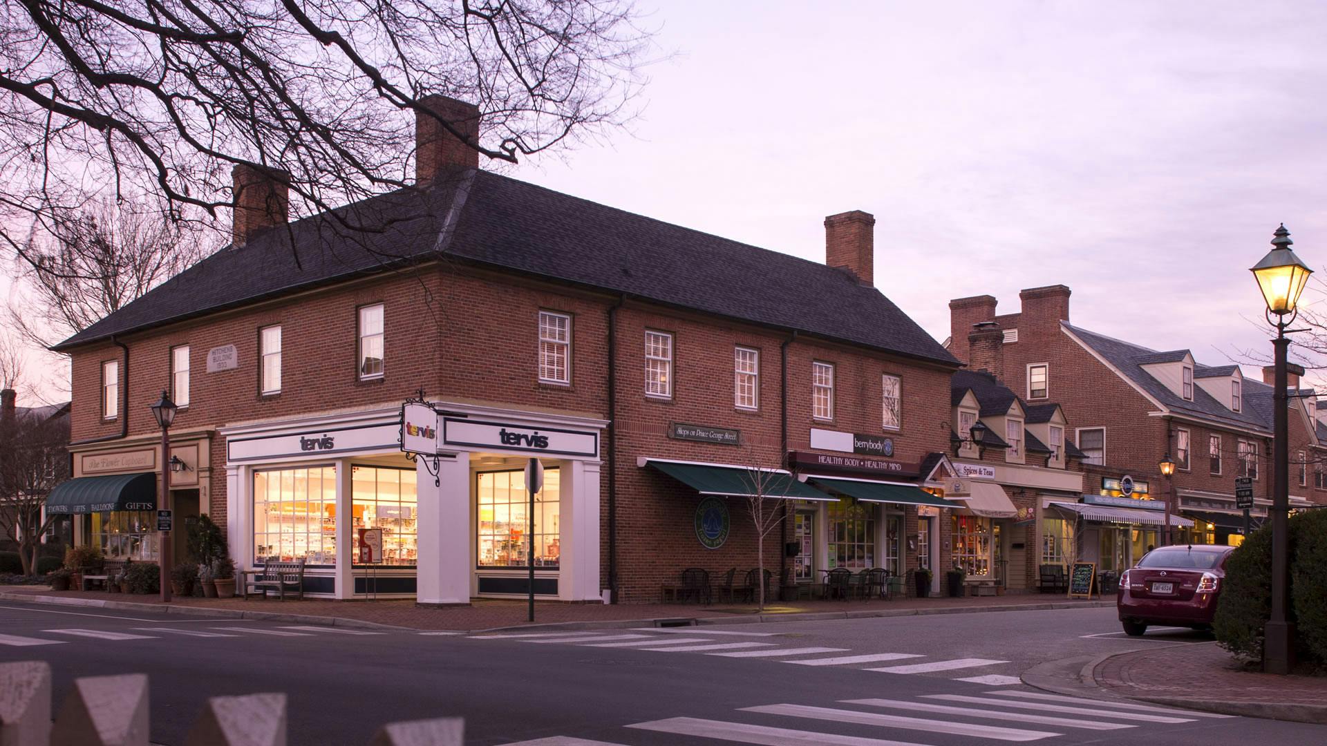 A series of colonial red brick storefront buildings with several tall chimneys.