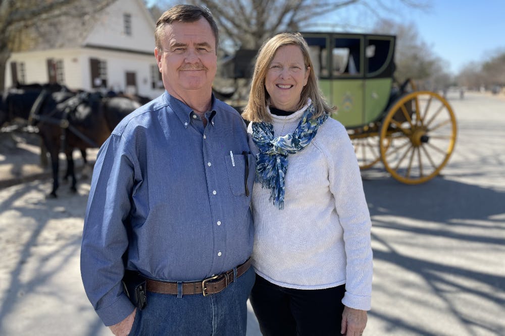 A smiling man and woman in front of a horse drawn carriage