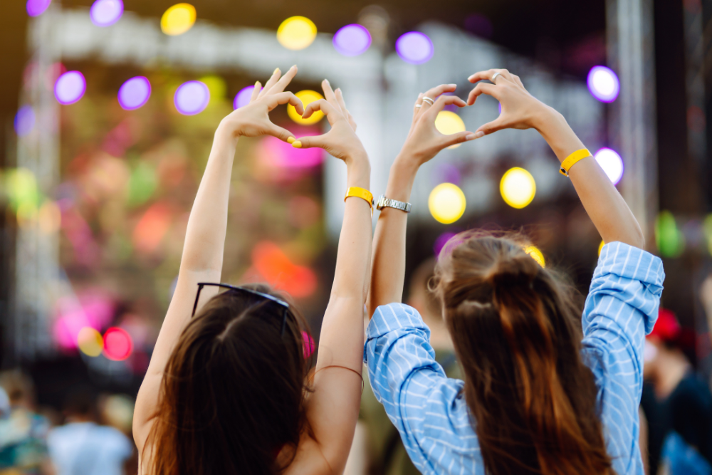 Two people at a concert making hearts with their hands above their heads. 