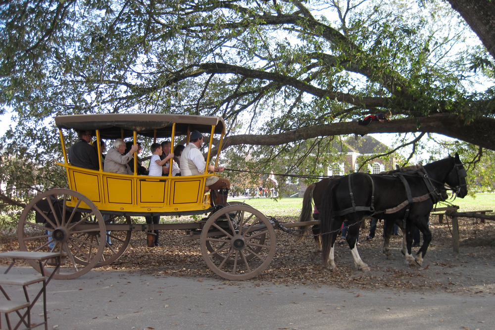 Many people in a yellow wagon with a roof being pulled by 2 brown horses.