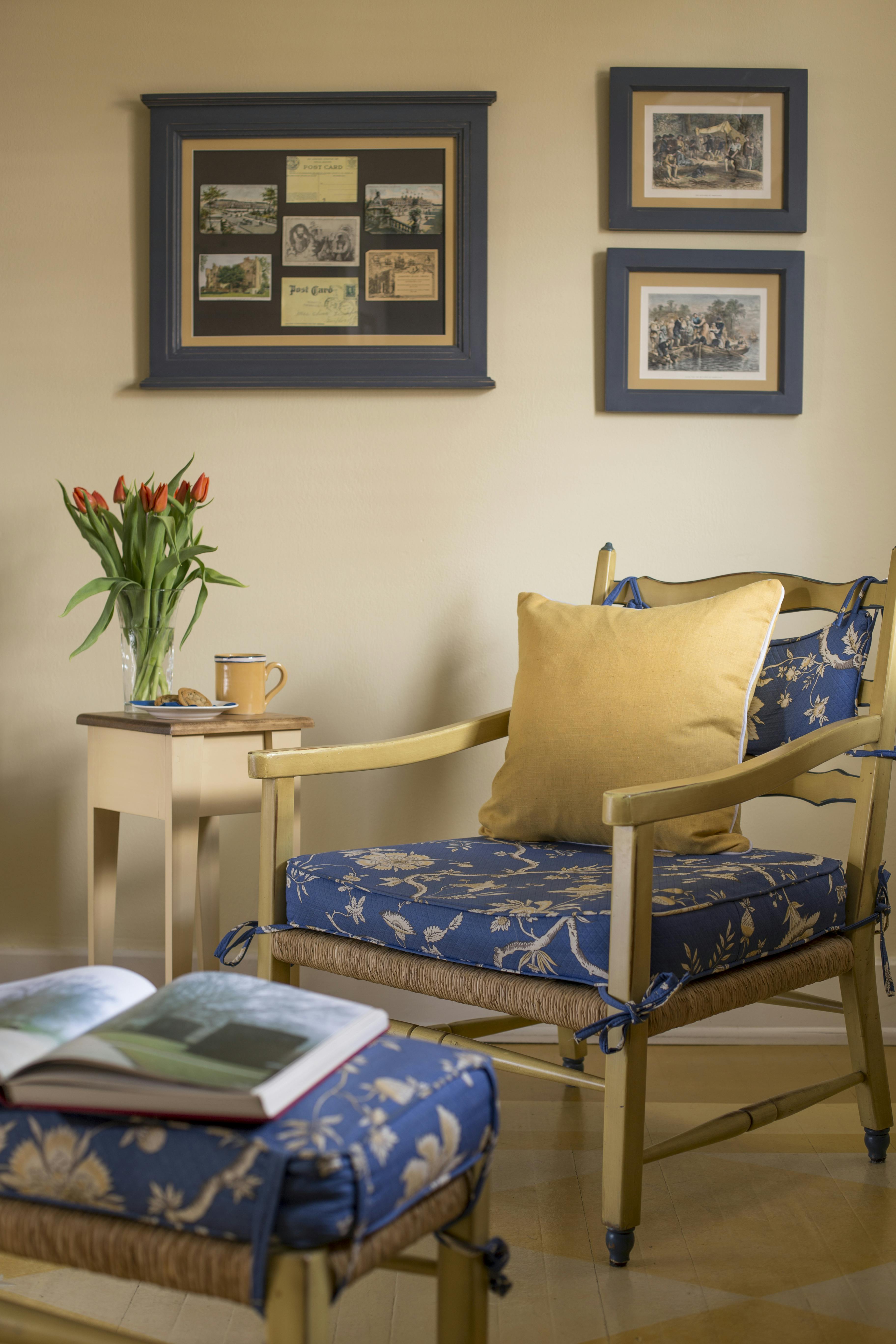 Wooden chair with blue and yellow cushions and matching footstool, small occasional table with mug and vase of tulips