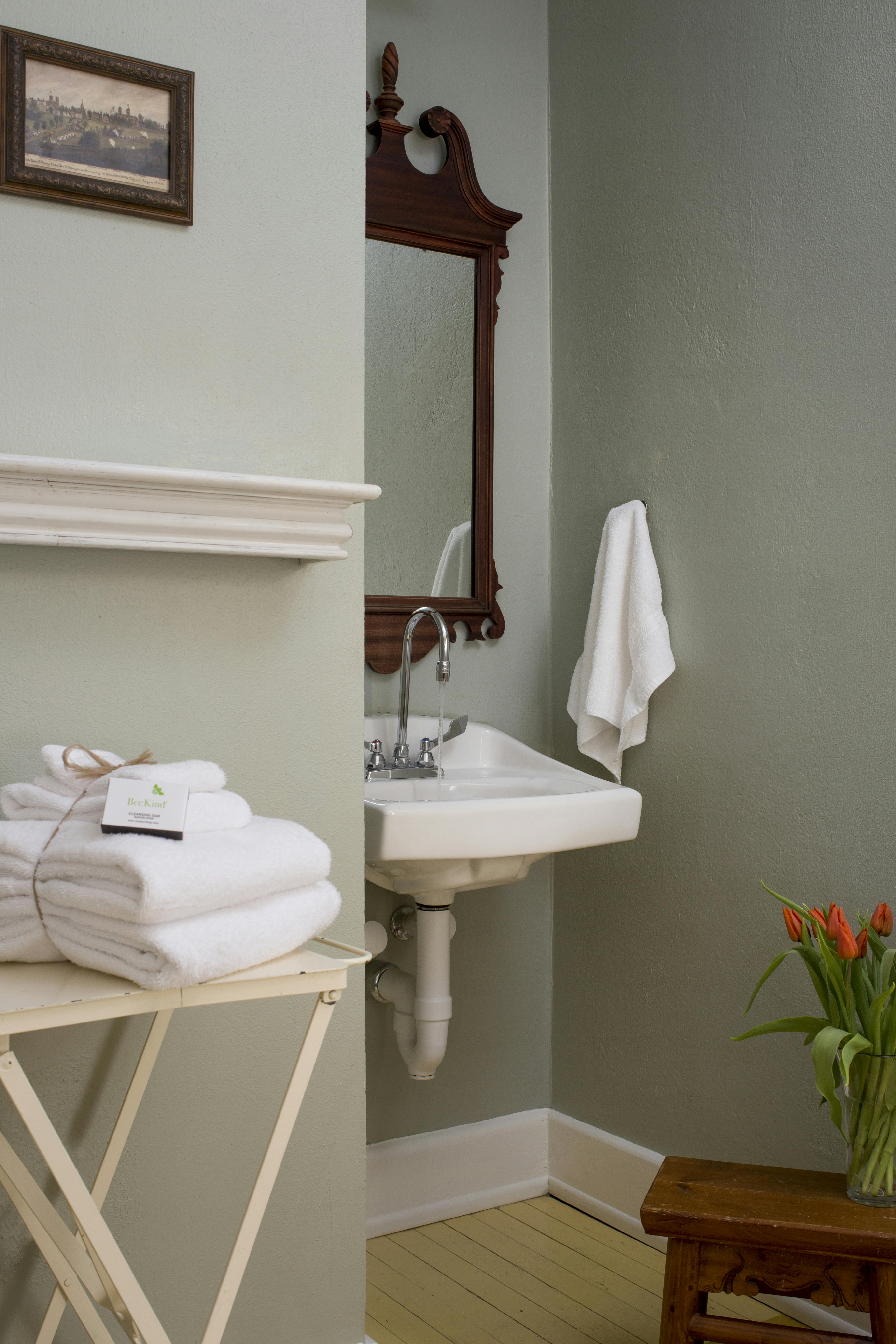 Wall-mounted sink with white plush towels on stand nearby, beautifully framed mirror above