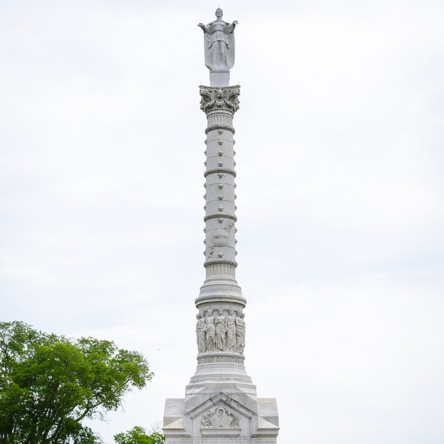 A tall stone monument with a woman with outstretched arms on the top