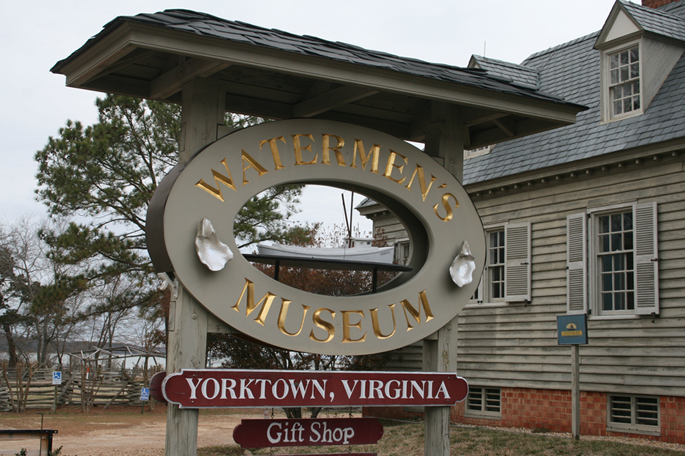 Round watermans museum sign in front of cream wood shingle 2 story building