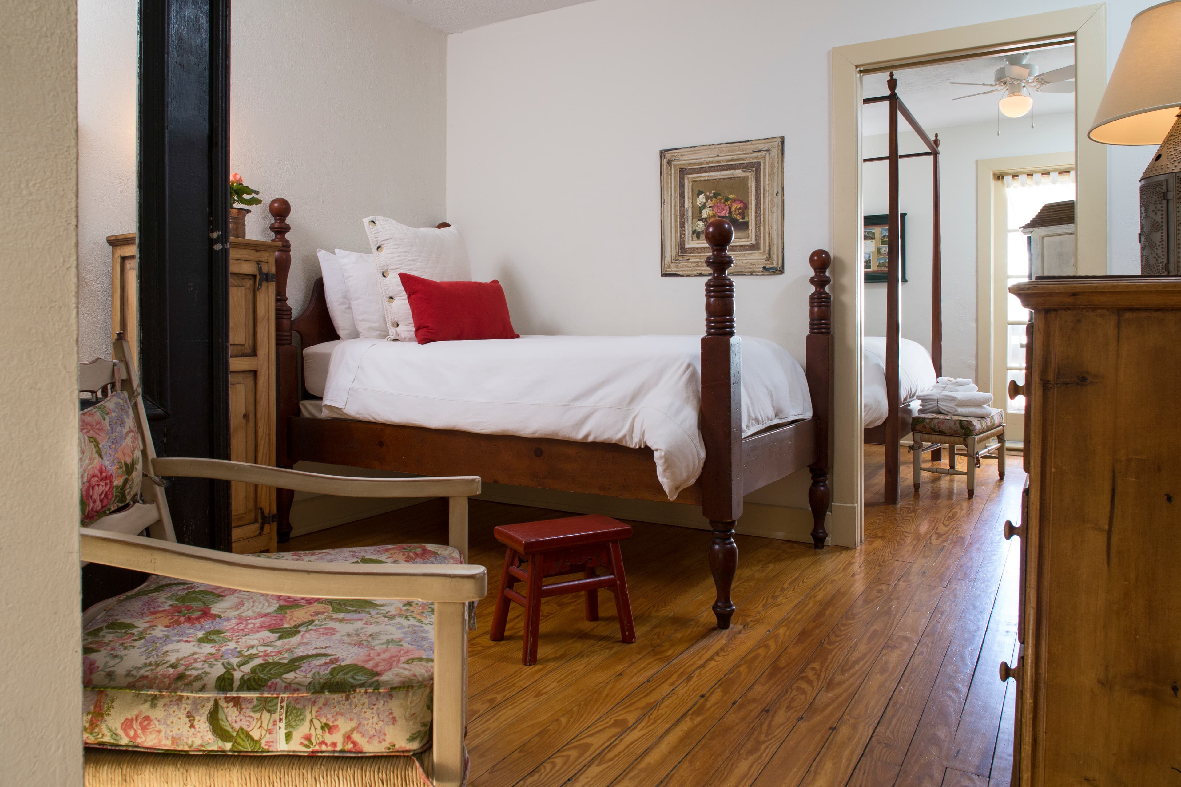 Bedroom with wooden chair with floral cushions, four-poster bed, hardwood floors, doorway into second bedroom
