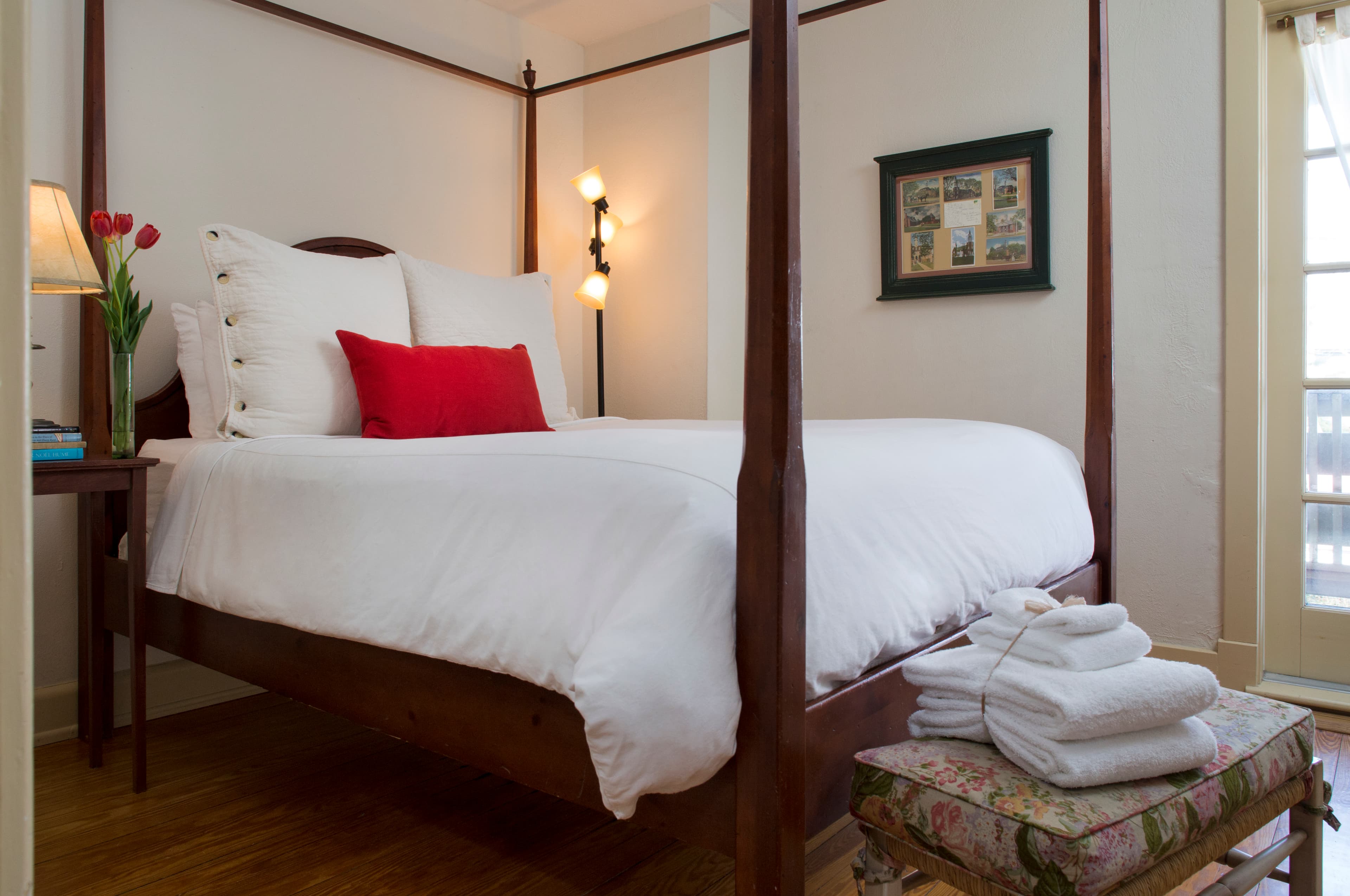 Tall four-poster bed, bench with cushion and extra towels, side table with lamp