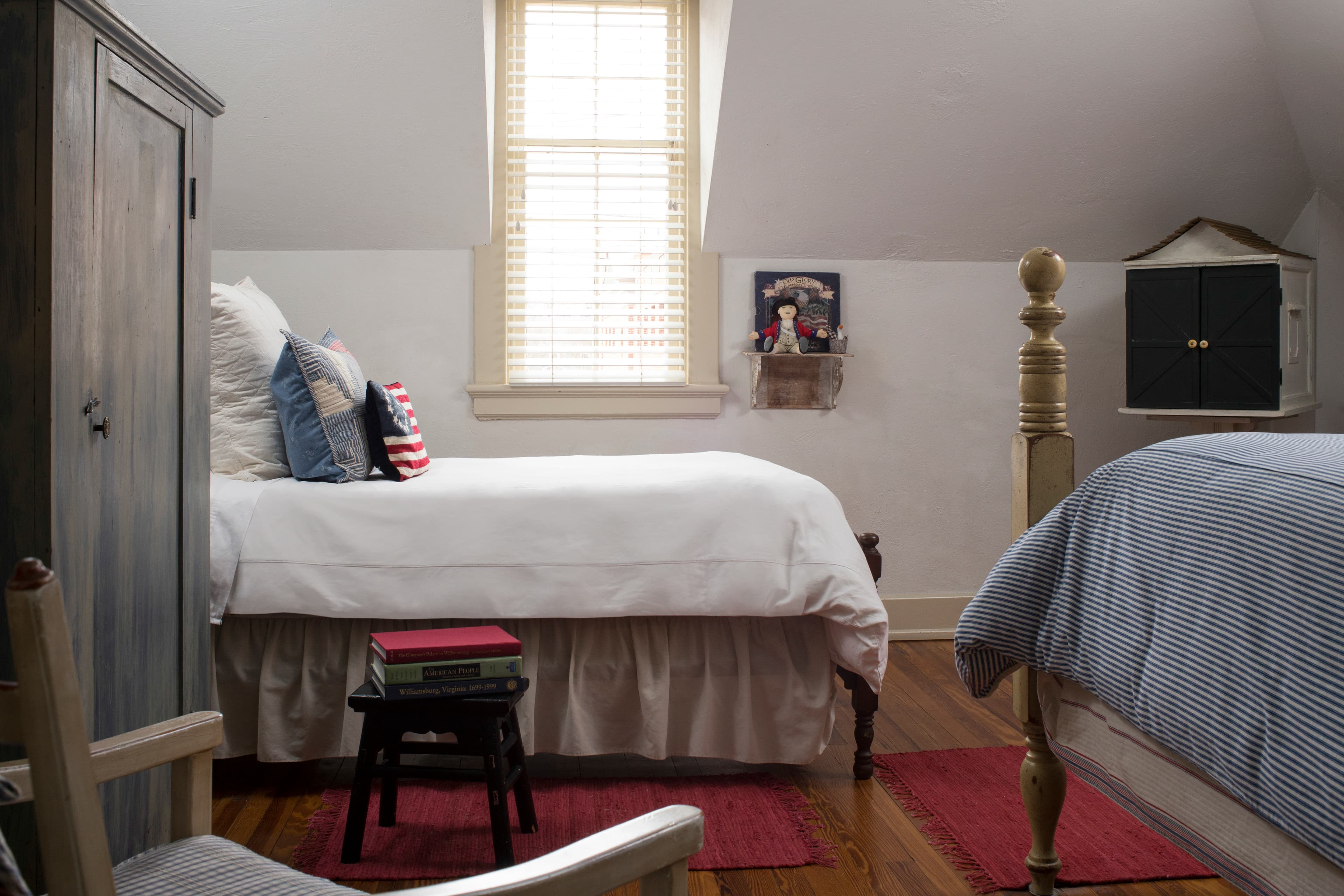 Bedroom with two beds, wooden chair with cushion, painted armoire and beautifully stained wood floors