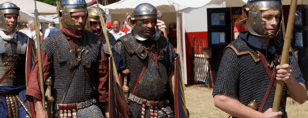 A group of men dressed in historical Roman soldier attire, complete with helmets and armor, walking together.