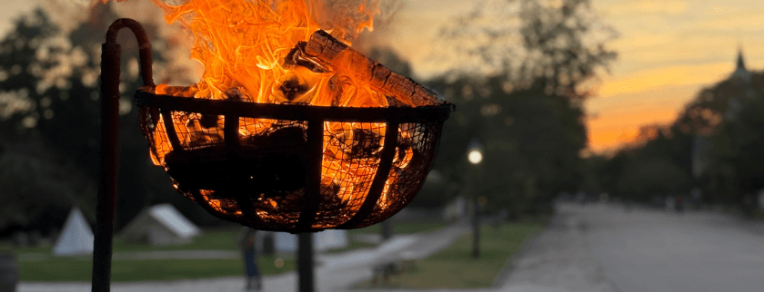 A glowing fire in a basket against a dusk sky along a park path.
