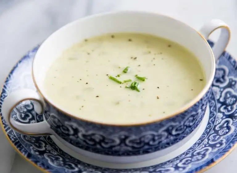 A bowl of creamy soup garnished with chopped herbs, served on a decorative plate.