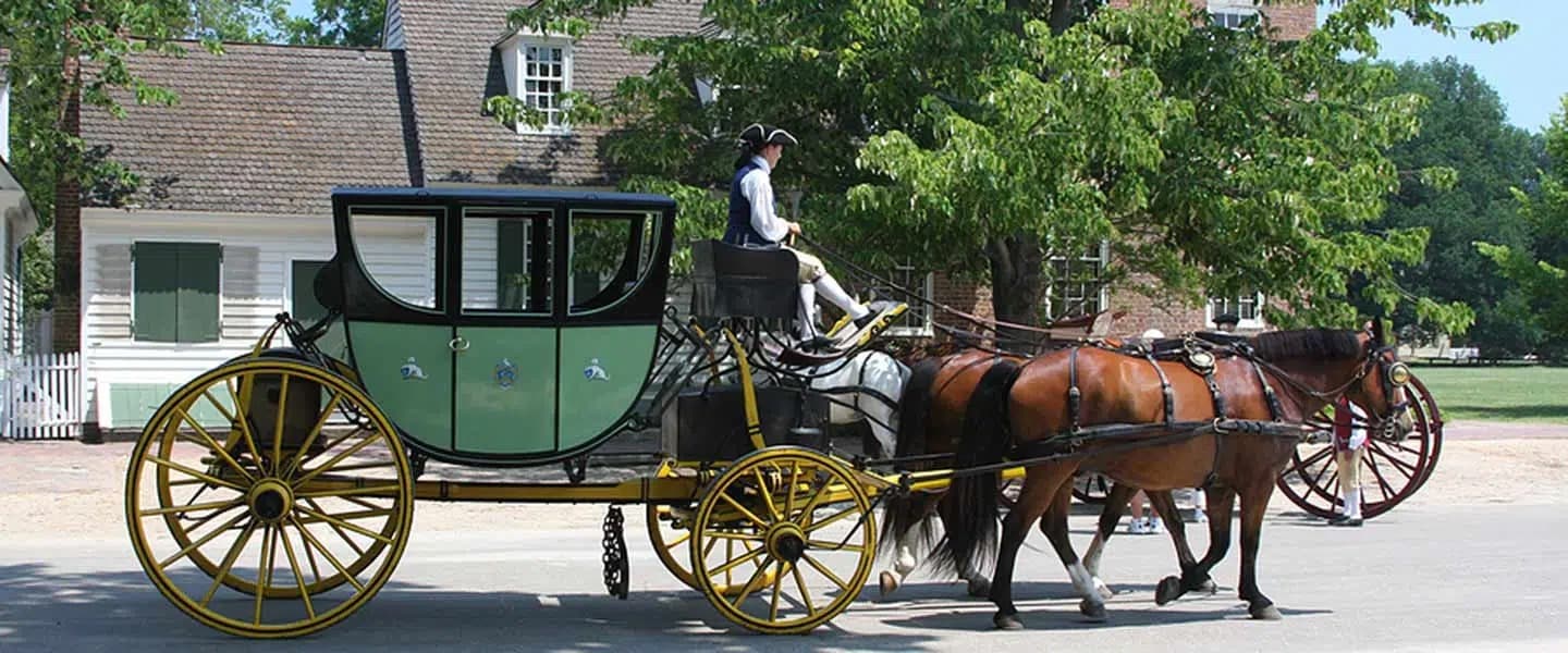 A horse-drawn carriage with a driver passes by in a leafy, historic setting. A horse-drawn carriage with a driver passes by in a leafy, historic setting.
