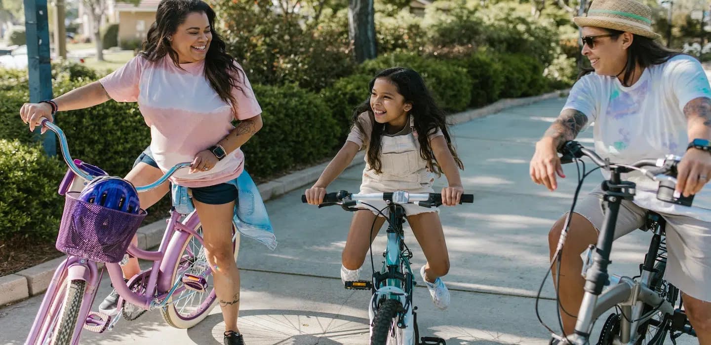 Two adults and a child joyfully ride bicycles along a park pathway.