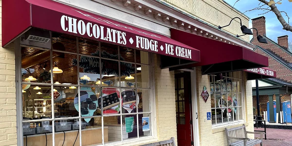 A storefront featuring a maroon awning that advertises chocolates, fudge, and ice cream.
