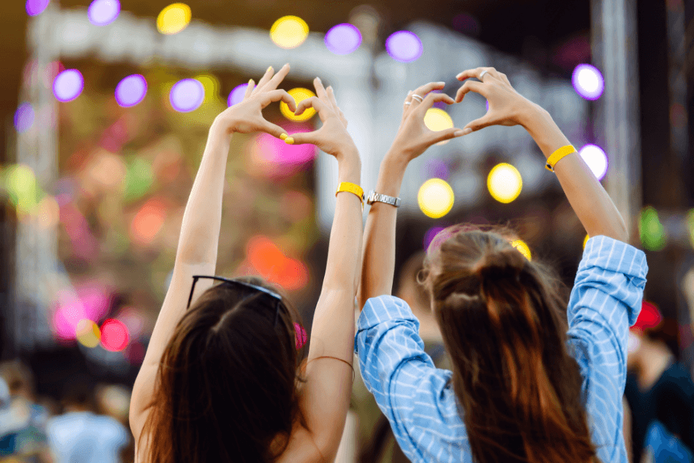 Two people at a concert making hearts with their hands above their heads.