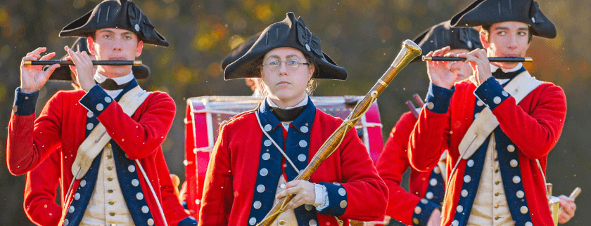 A group of musicians in Revolutionary War-era uniforms playing flutes.