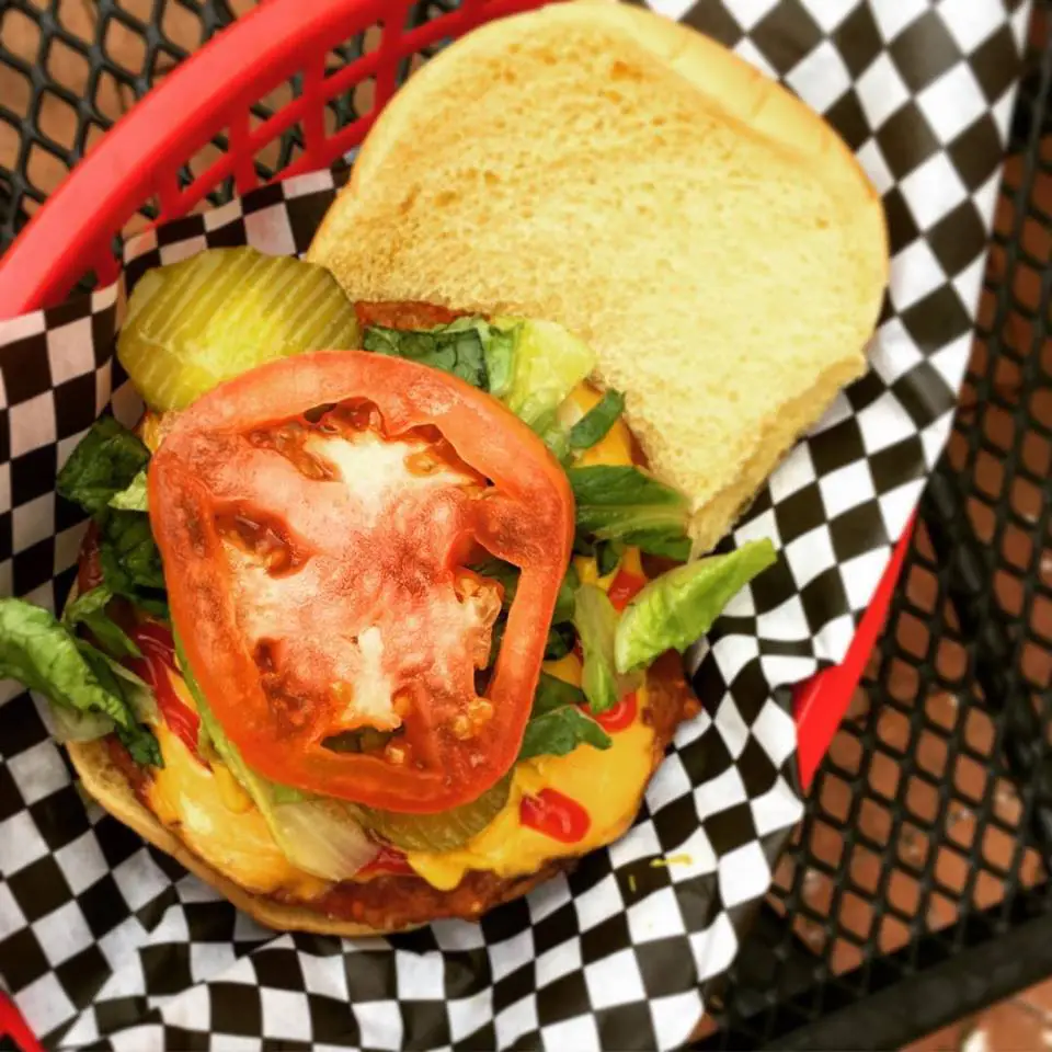 A close-up of a cheeseburger with lettuce, tomato, pickles, and ketchup in a red basket.