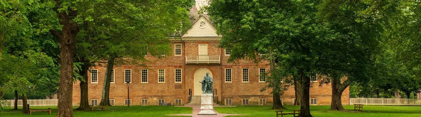 A historic brick building surrounded by lush green trees, featuring a statue in front. A historic brick building surrounded by lush green trees, featuring a statue in front.