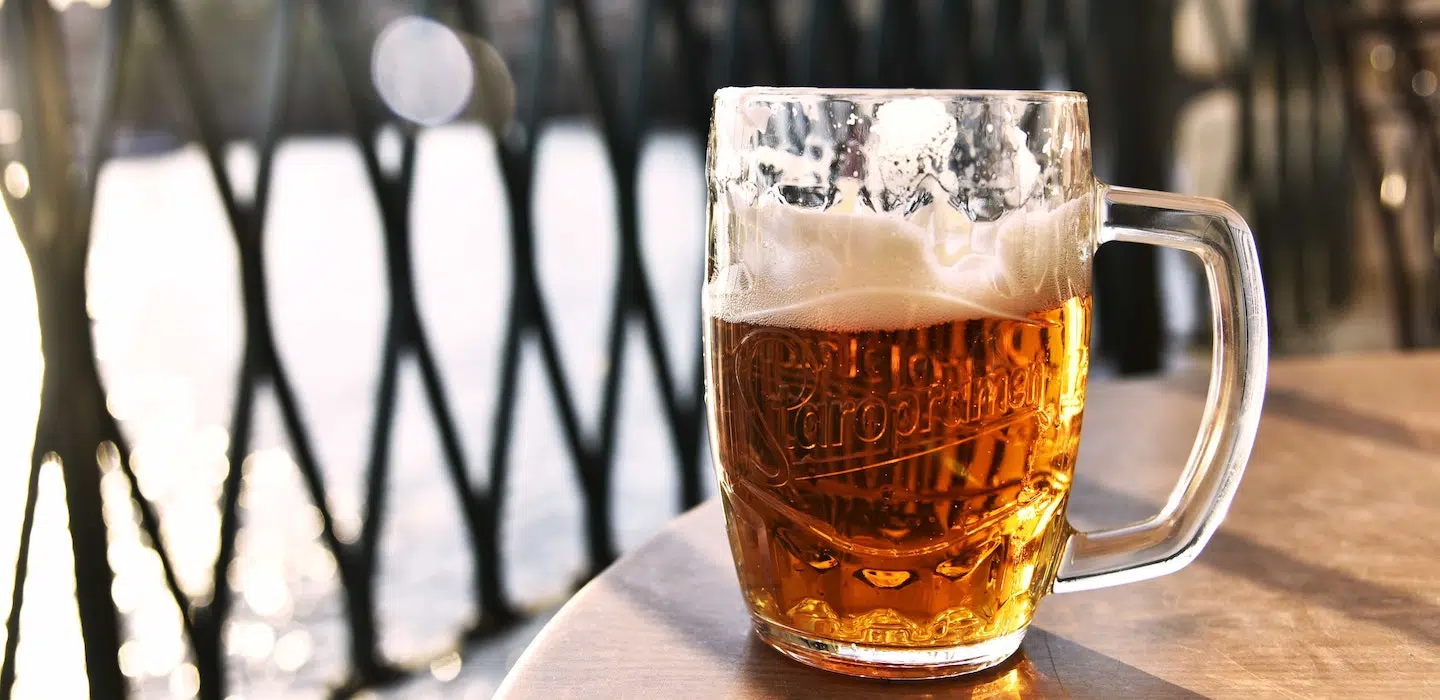 A frosty glass of beer sits on a wooden table with a blurred background.