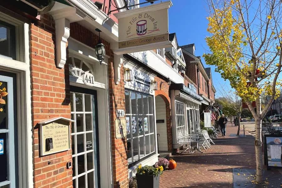 Exterior view of a brick storefront labeled "The Ice & Drink Inn" on a sunny day, with trees and people nearby.