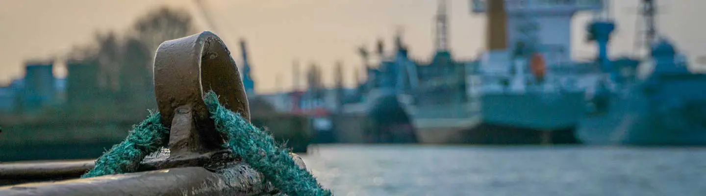 A close-up of a mooring ring with green rope, blurred ships in the background. A close-up of a mooring ring with green rope, blurred ships in the background.