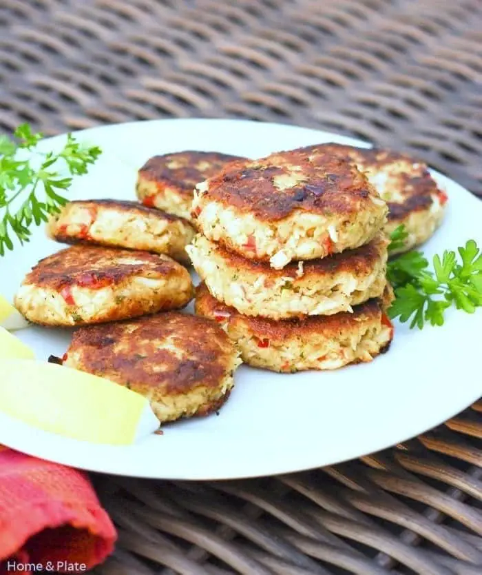 A plate of golden-brown crab cakes garnished with fresh herbs and lemon slices.