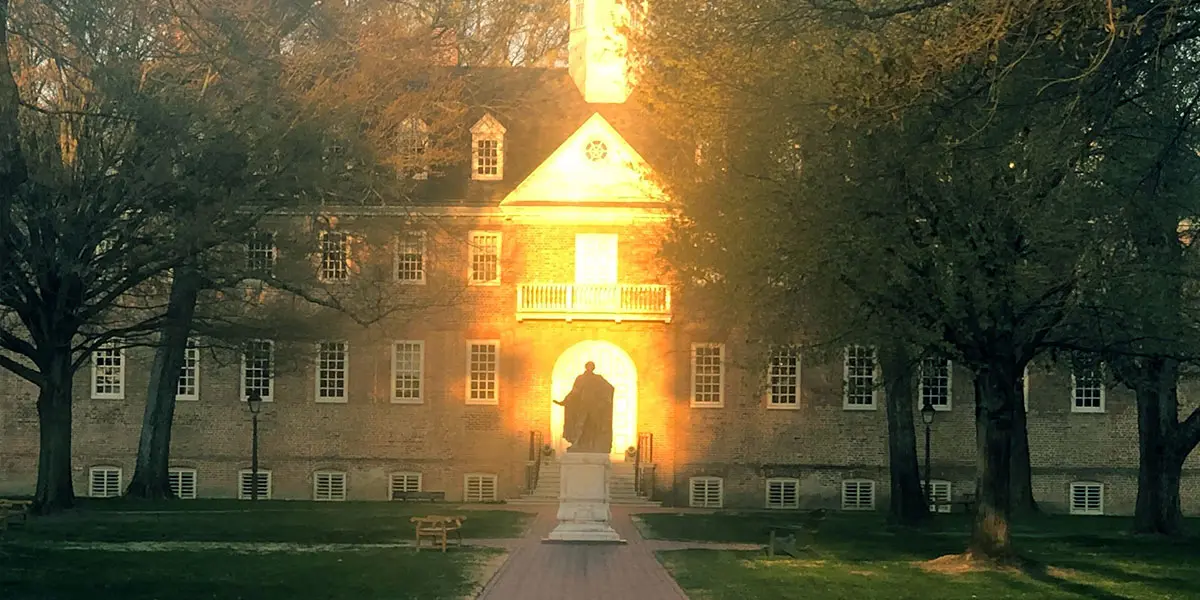 Historic building illuminated by sunset, featuring a central statue and surrounded by trees.