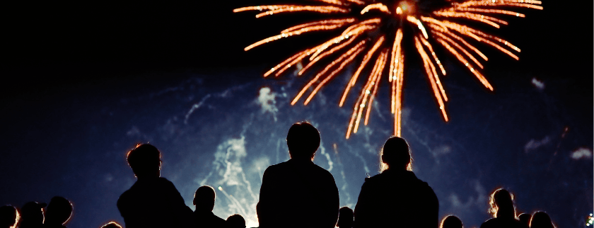 Silhouettes of people watching a fireworks display at night.