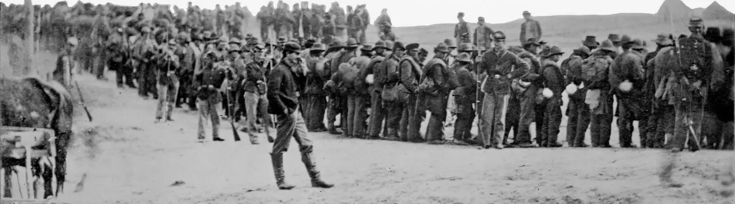 A historical image of a large group of soldiers lined up, with one soldier walking in front. A historical image of a large group of soldiers lined up, with one soldier walking in front.