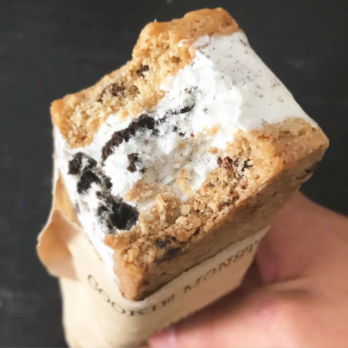A bitten cookie sandwich filled with creamy filling and chocolate pieces.