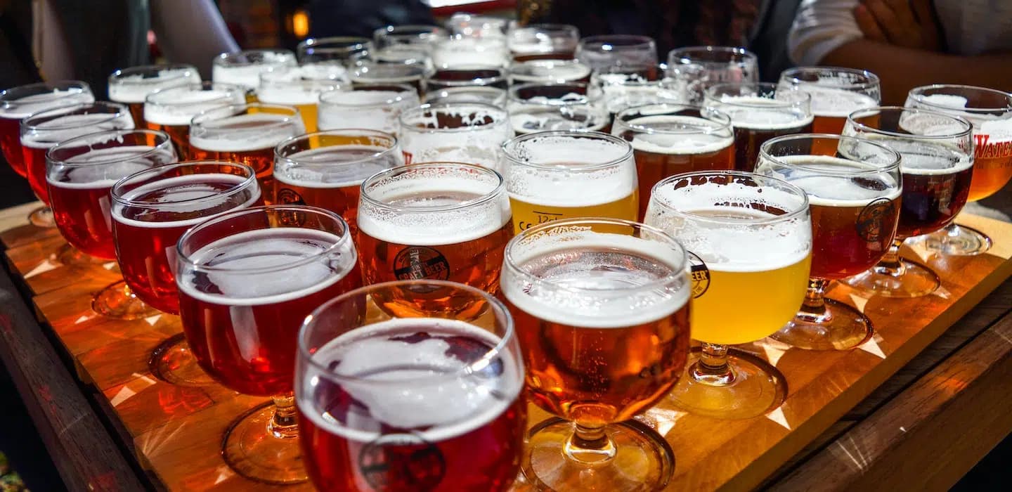 A variety of craft beers in small glasses arranged on a wooden tray.