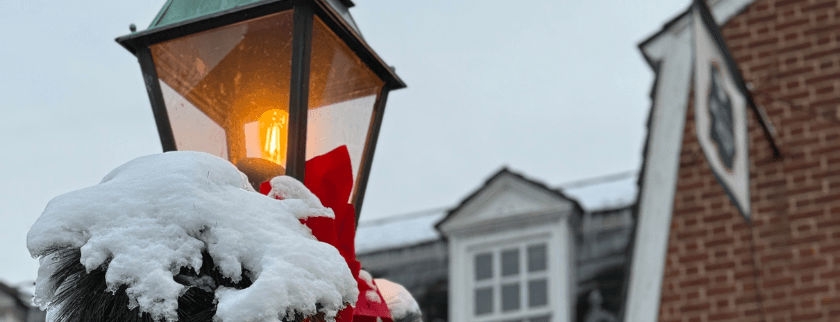 A snowy lantern adorned with a red ribbon glows against a muted winter backdrop.