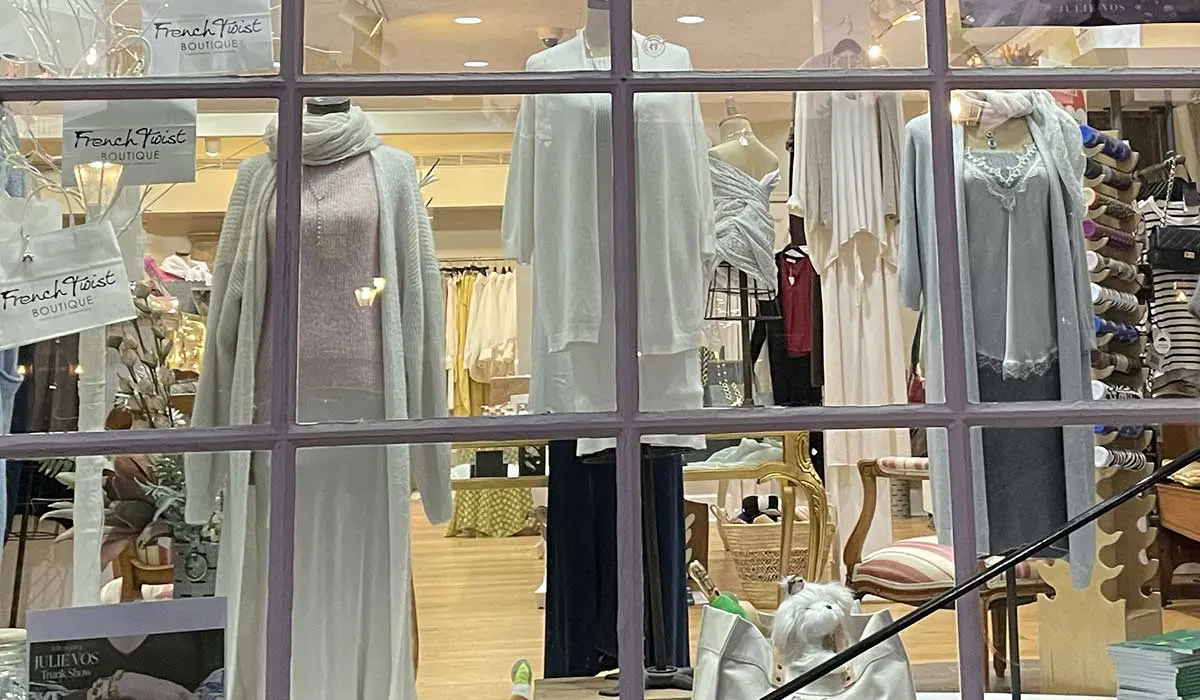A boutique window display featuring various light-colored clothing items and a decorative bear.
