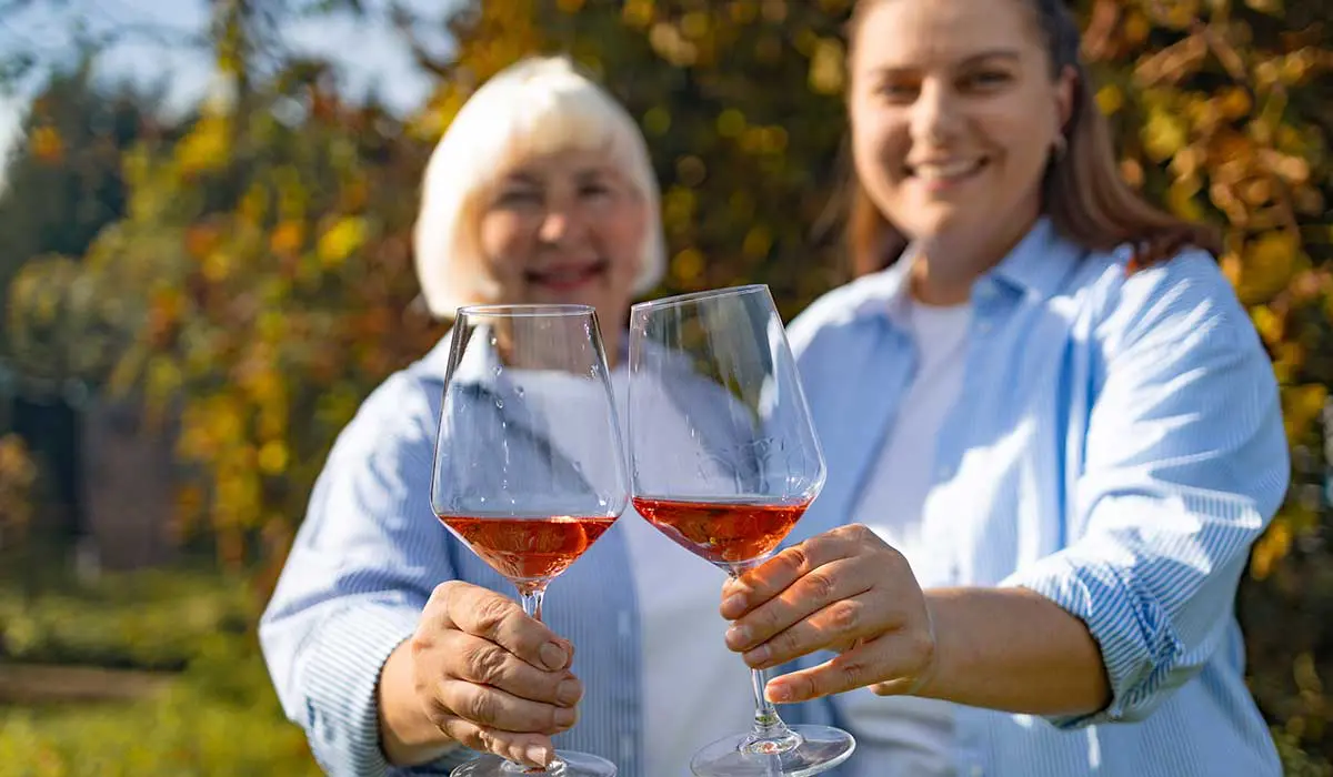 Two women smiling and toasting with glasses of rosé wine outdoors.
