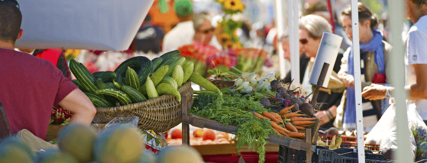 A vibrant farmers market with various fresh vegetables and people browsing.
