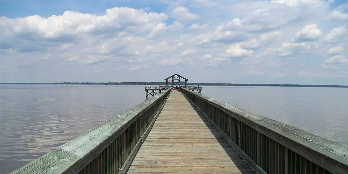 A wooden pier extends into calm water under a cloudy sky.