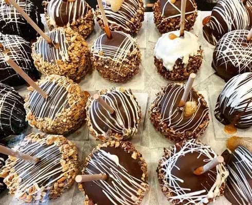 A variety of chocolate-covered caramel apples with toppings and decorative drizzles arranged on a tray. A variety of chocolate-covered caramel apples with toppings and decorative drizzles arranged on a tray.