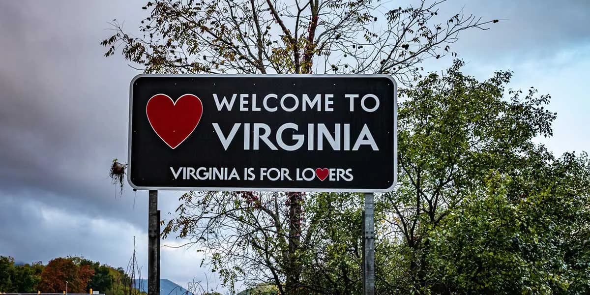 Black and white welcome sign for Virginia surrounded by greenery, featuring a heart and the phrase "Virginia is for lovers."