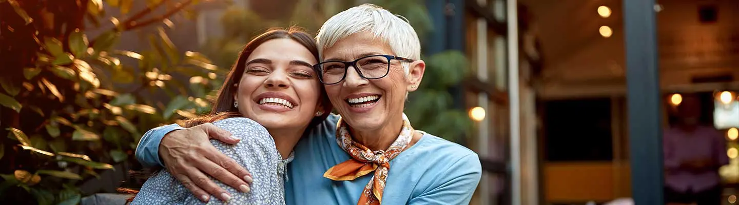 A young woman and an older woman embrace and smile joyfully in a cozy outdoor setting. A young woman and an older woman embrace and smile joyfully in a cozy outdoor setting.