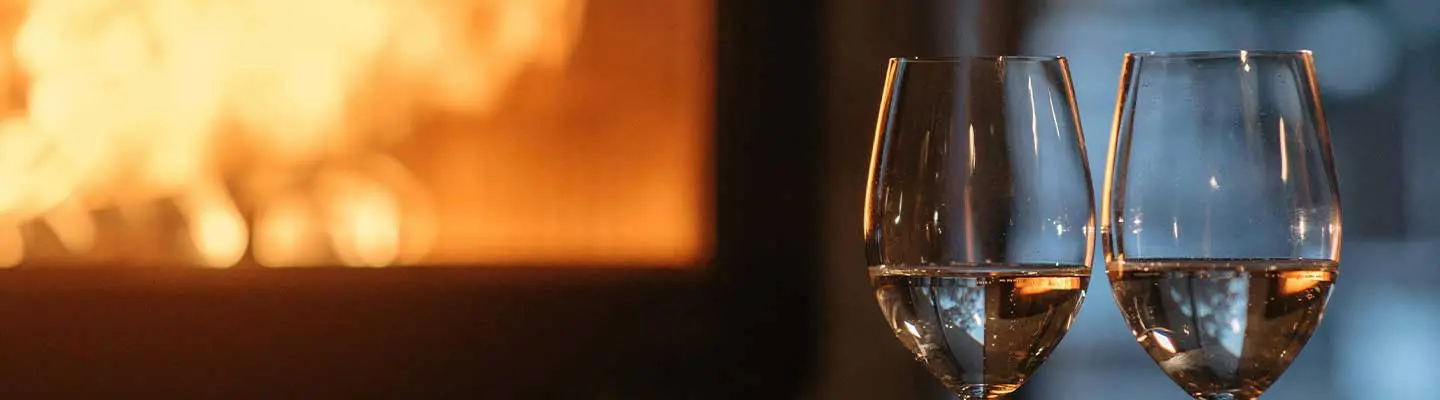 Two glasses of wine in front of a glowing fireplace.