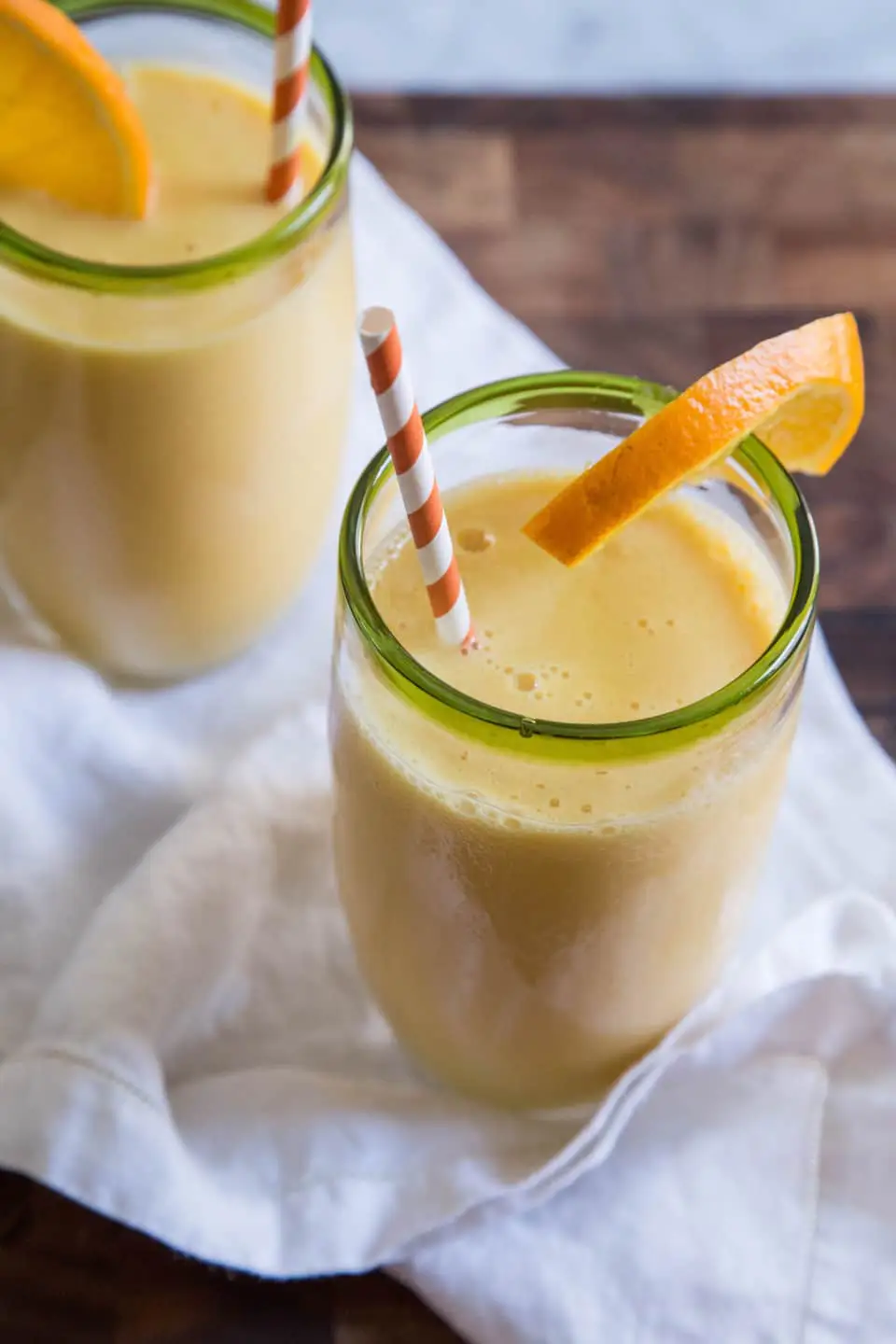 Two glasses of smoothie topped with orange slices and striped straws.