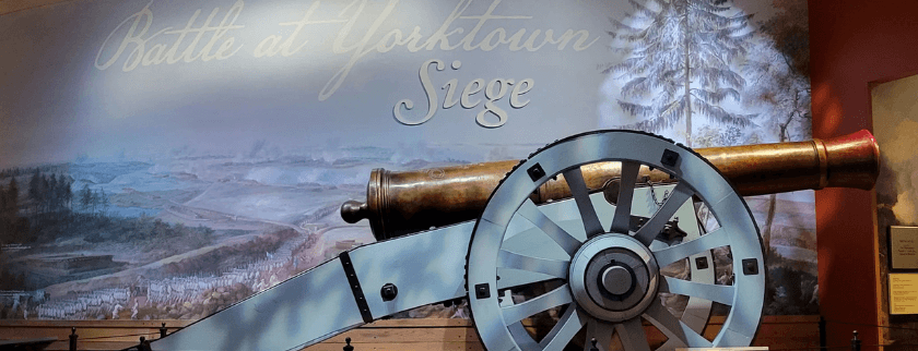 A historic cannon displayed against a backdrop depicting the Siege of Yorktown.