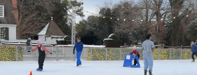 A group of people ice skating on an outdoor rink decorated with lights.